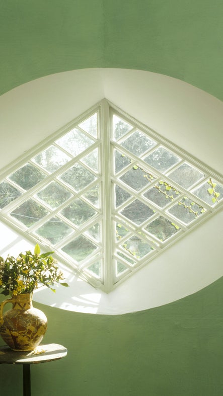 Light coming through a diamond-shaped window at A la Ronde, Devon, and a jug with flowers stands on a small table.